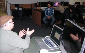 Lecturer gestures, his hands reflected in a computer screen.