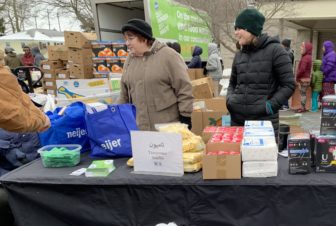 Two women stand behind a table piled with feminine hygiene products.