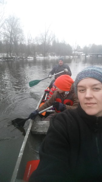 A white female taking a selfie of her family and herself while kayaking on the river.