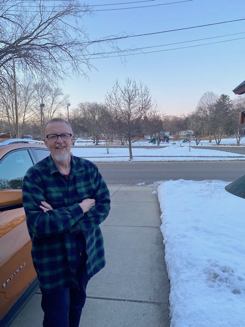 Roger Bauer stands in his driveway, across the street from a city park, smiling.