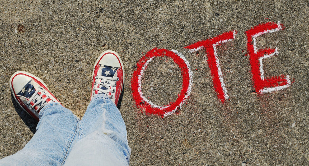 Sneakers form the V in the word vote chalked on pavement