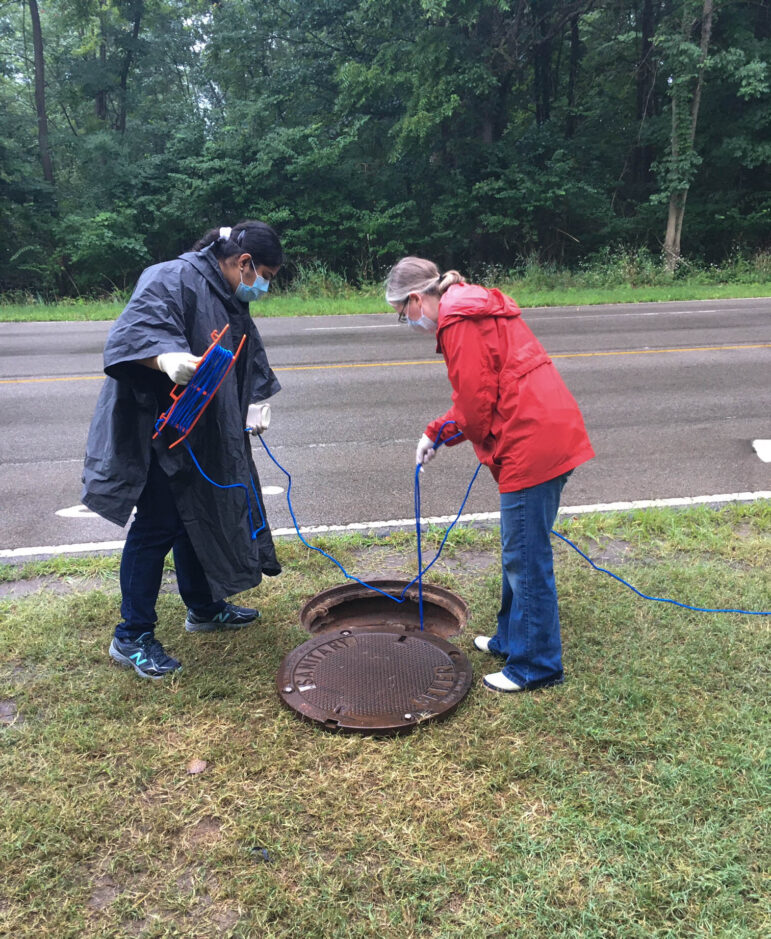  Researchers Becca Ives and Nishita D’Souza lower a container into a manhole to sample wastewater at Michigan State University.