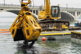 An excavator drops activated carbon into the Detroit River.