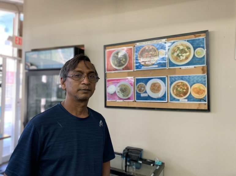 Owner Moe Israel poses in front of his menu, which is currently only available throughout takeout. The focus on serving traditional, home-style food consistently has made Naing Myanmar Family Restaurant a local favorite in south Lansing.