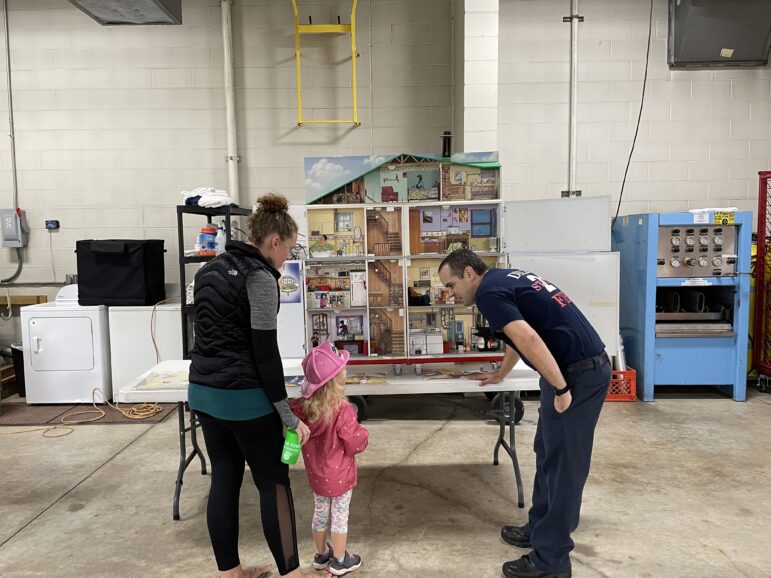 firefighter shows off a model of a house to a little girl