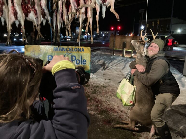 Joanie Moore takes a picture of a hunter hugging his buck at the base of the buck pole in Mancelona.