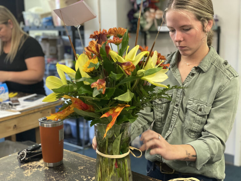 Inside Wild Strawberry and More, a florist shop in Holt, delivery driver Jessa Powers ties a ribbon around a floral arrangement. Powers has taken on more responsibilities as the business has adapted to the pandemic.