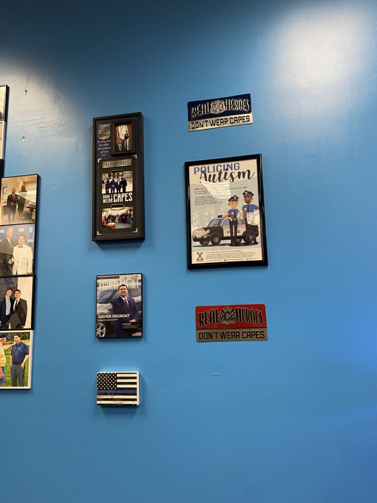 A Blue Lives Matter Flag, various posters saying "Real Heroes Wear Capes" and a poster about "policing autism" is on the wall