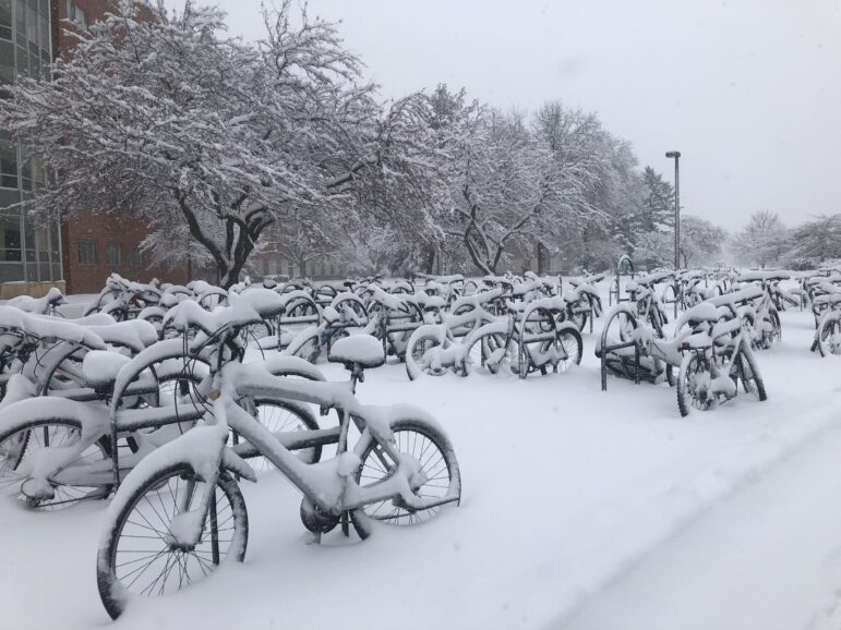 Snow covers bikes at racks.