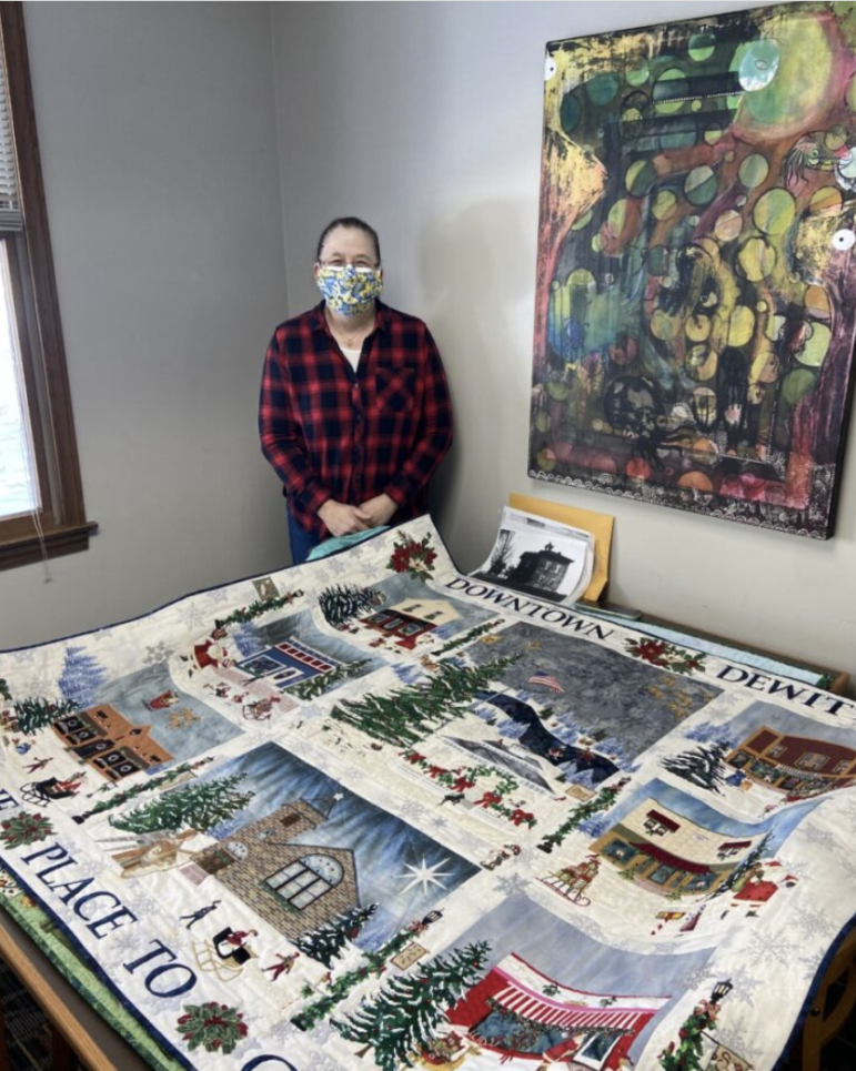 Artist stands behind quilt on table.