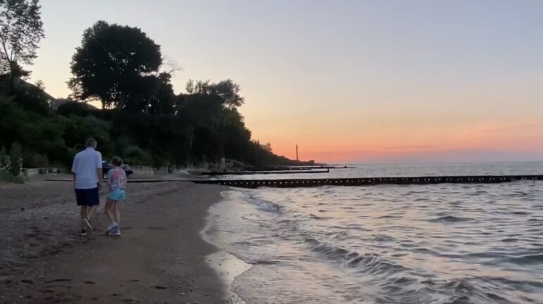 A father and daughter walk along Lake Michigan at sunset.