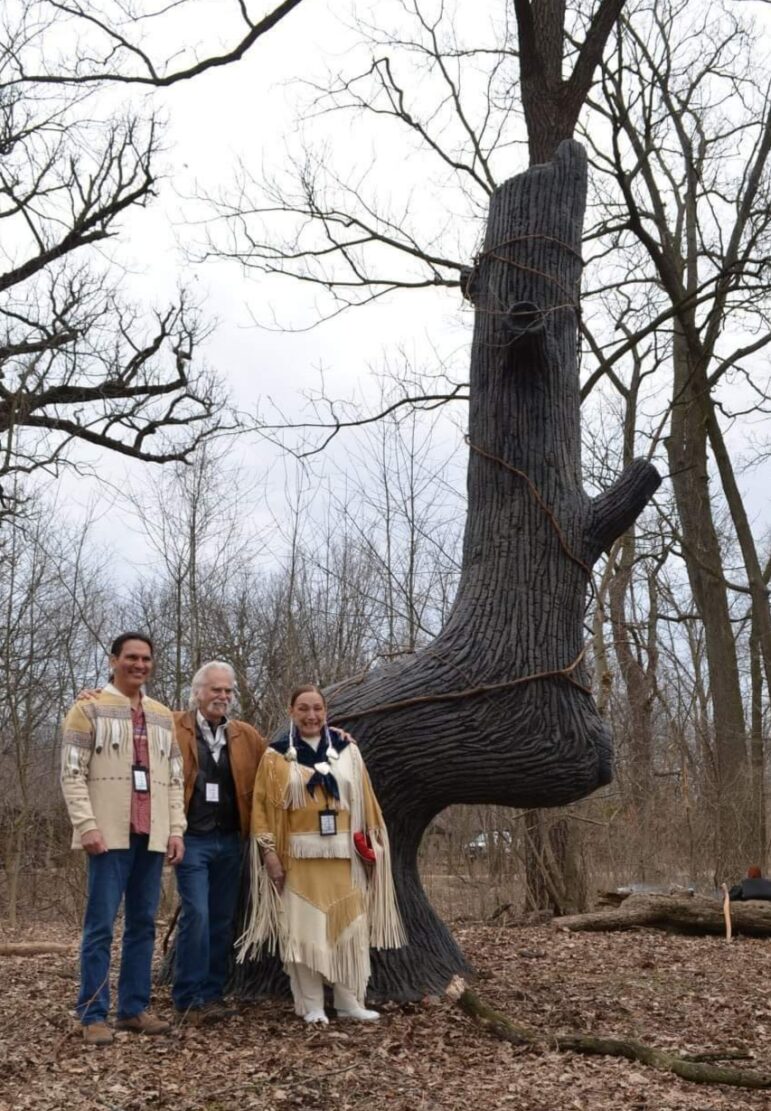 Dennis Downes, center, with the 16-foot sculpture of a trail tree that he made in Glenview, Illinois in 2021. He is standing with Cherokee Elder Andrew Johnson and Ottawa Elder Hilda ‘Little Fawn’ Williams.