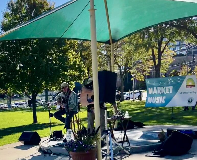 Man plays guitar under awning in park.