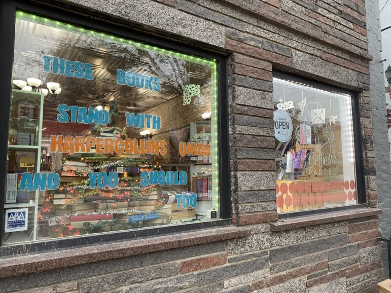 A colorful window sign outside of a bookshop reads, "these books stand with HarperCollins Union and you should too."