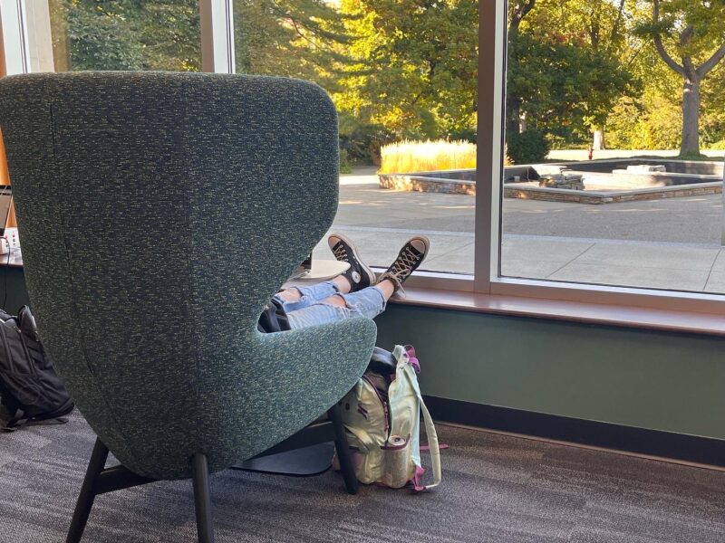 A student sits in a chair with their feet resting on a window sill Inside the MSU main library