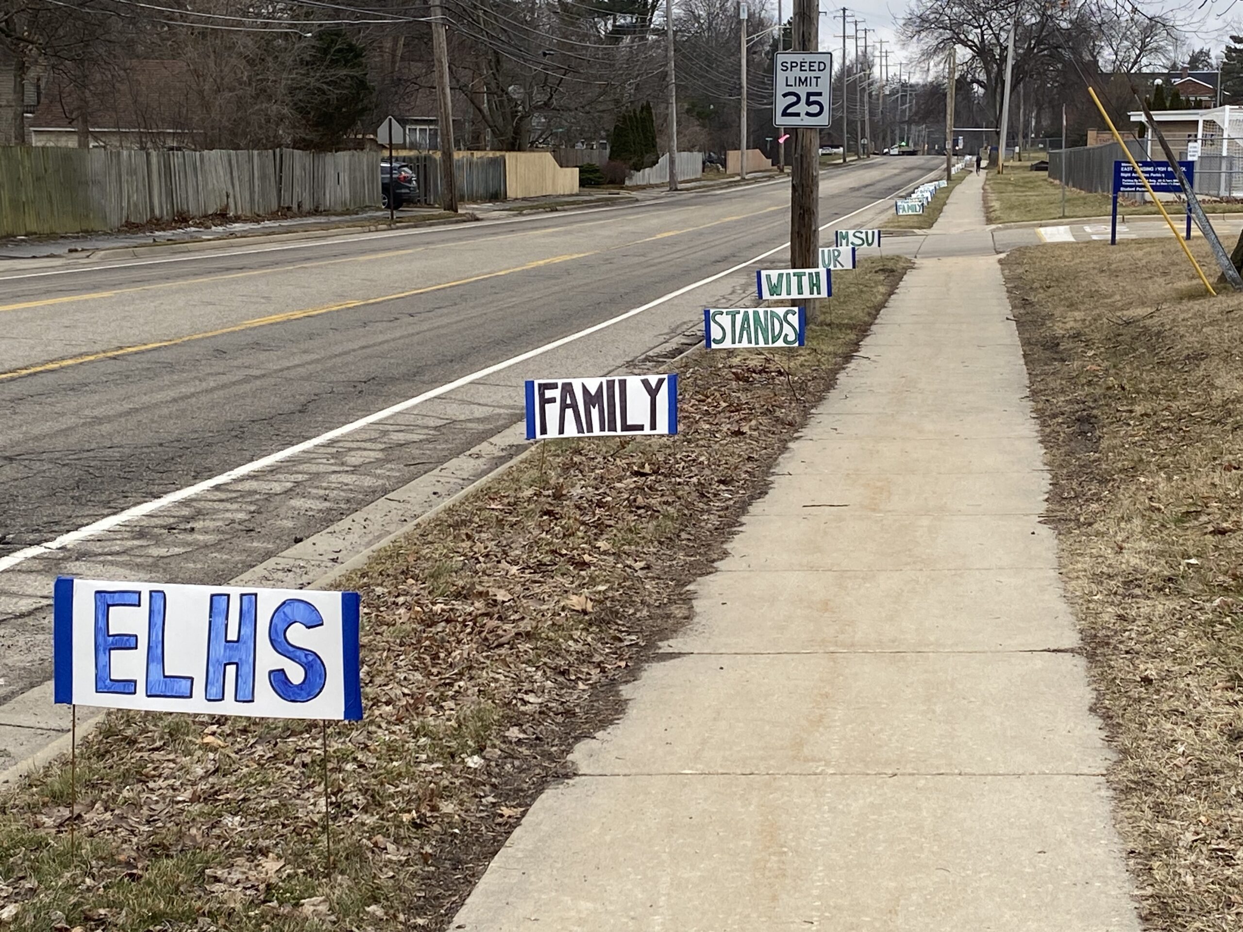 signs along the sidewalk that say ELHS. Family. Stands. With. MSU