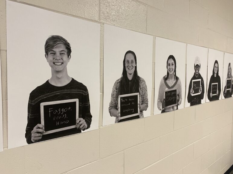 Posters of students holding chalkboards with insults line a school wall.