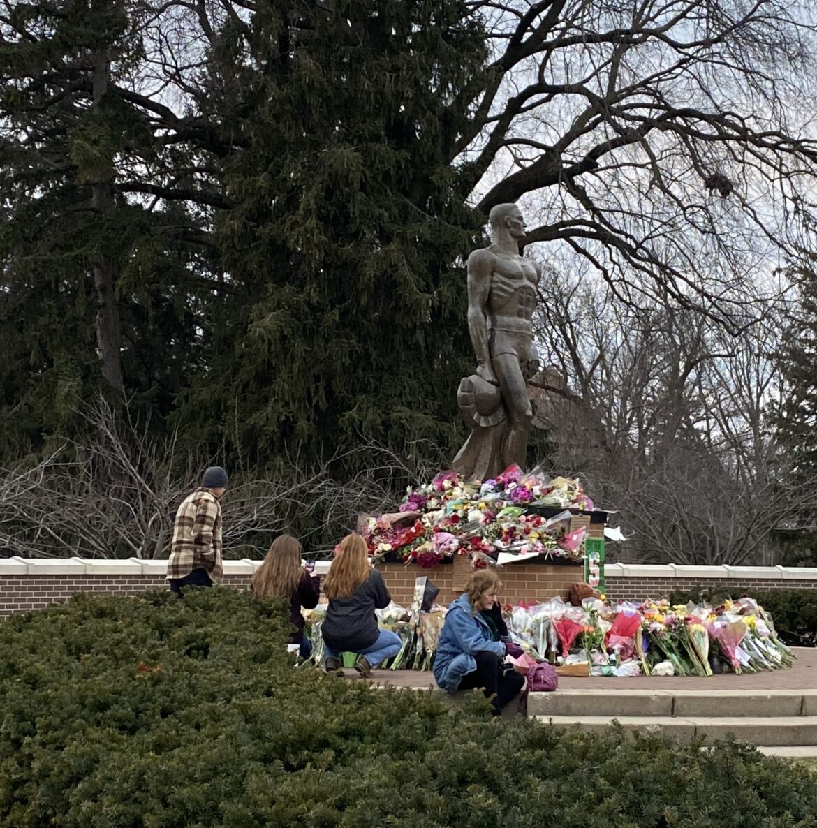 Community members leave flowers at the Spartan Statue on the Michigan State University campus