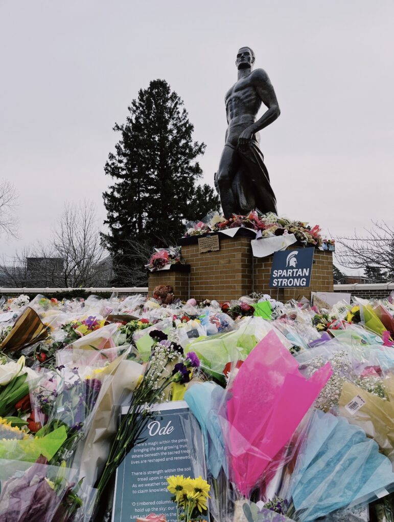 The Spartan Statue surrounded by flowers and signs.