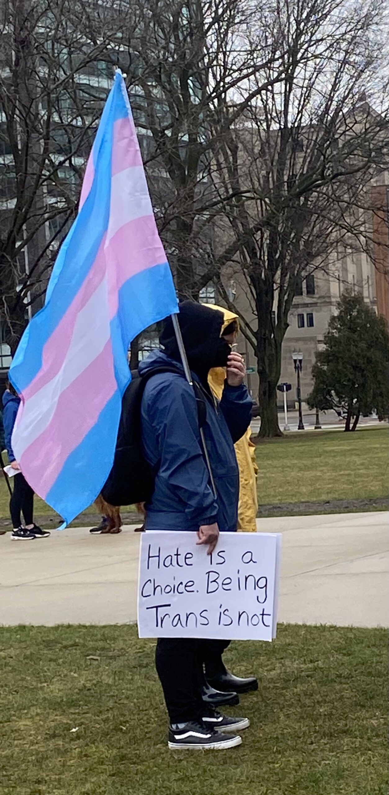 Activist holding a transgender flag (blue, pink, and white) and a sign that says "hate is a choice. being trans is not."