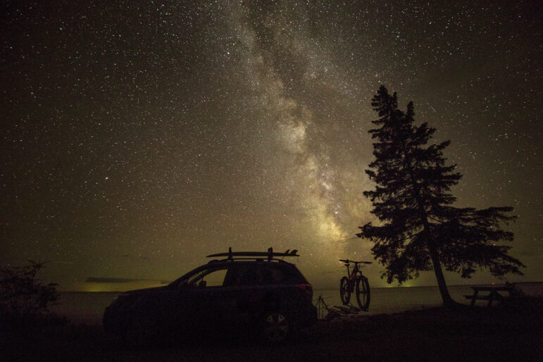 A visitor’s car and bike are silhouetted against the night sky at the Upper Peninsula’s Keweenaw Dark Sky Park